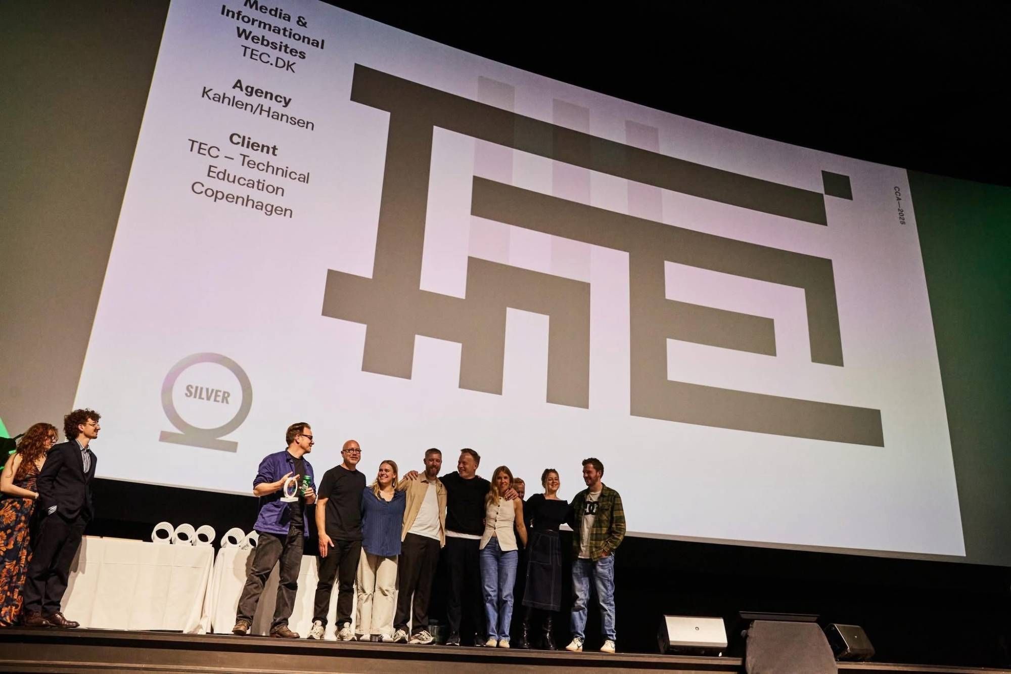 Holdet bag TEC.dk på scenen ved Creative Circle Awards 2025 foran storskærmen med TECs supergrafik og sølvprisen i Media & Informational Websites