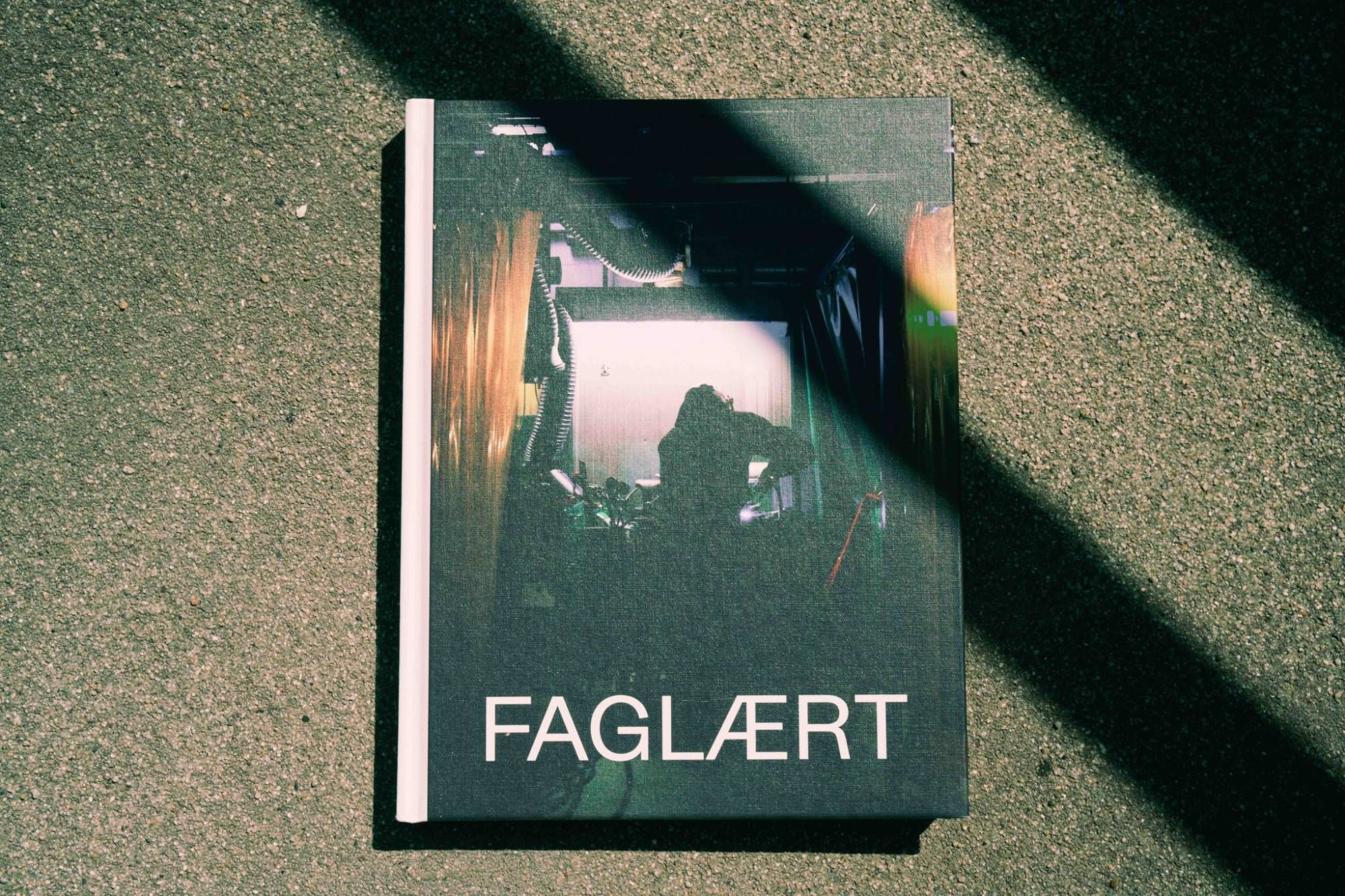 Fotobogen FAGLÆRT med et mørkt, grønligt værkstedsbillede på forsiden, fotograferet i skarpt sollys